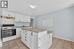 Kitchen featuring white range with electric cooktop, light countertops, light tile patterned floors, white cabinets, and under cabinet range hood - 