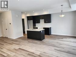 Kitchen with dark cabinetry, recessed lighting, a center island with sink, pendant lighting, and light wood-type flooring - 