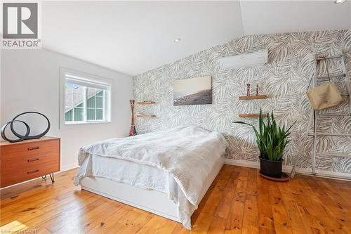 Bedroom with wallpapered walls, lofted ceiling, wood-type flooring, an accent wall, and an AC wall unit - 197 Cedar Drive, Turkey Point, ON - Indoor Photo Showing Bedroom