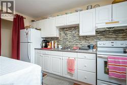 Kitchen featuring white appliances, under cabinet range hood, white cabinetry, and decorative backsplash - 