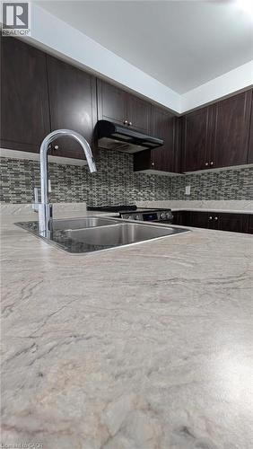 Kitchen with dark brown cabinetry, decorative backsplash, and under cabinet range hood - 19 Cromarty Avenue, Caledonia, ON - Indoor Photo Showing Kitchen With Double Sink