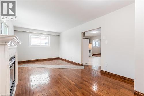 Unfurnished living room featuring wood-type flooring, a glass covered fireplace, and baseboards - 2340 King Street E, Hamilton, ON - Indoor Photo Showing Other Room