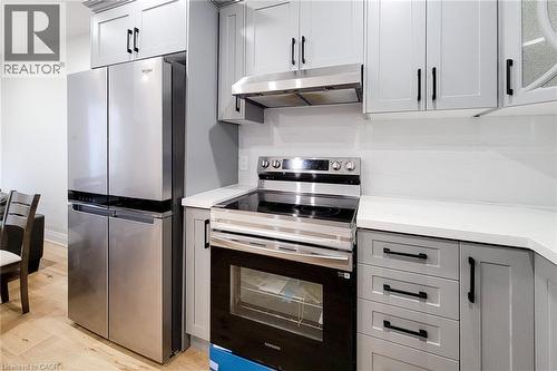Kitchen with stainless steel appliances, gray cabinets, under cabinet range hood, and light wood-type flooring - 51 West Avenue N, Hamilton, ON - Indoor Photo Showing Kitchen
