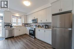 Kitchen with stainless steel appliances, backsplash, dark wood-style floors, and light stone countertops - 