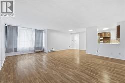 Unfurnished living room featuring wood finished floors and a baseboard heating unit - 