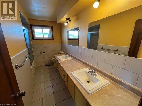 Bathroom with double vanity, dark tile patterned flooring, tile walls, a wainscoted wall, and shower / bath combination with glass door - 185 Lavina Crescent, Hamilton, ON - Indoor Photo Showing Bathroom