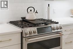 Kitchen view of gas range, backsplash, and white cabinets - 