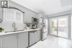 Kitchen featuring appliances with stainless steel finishes, gray cabinets, decorative backsplash, marble finish floor, and a sink - 