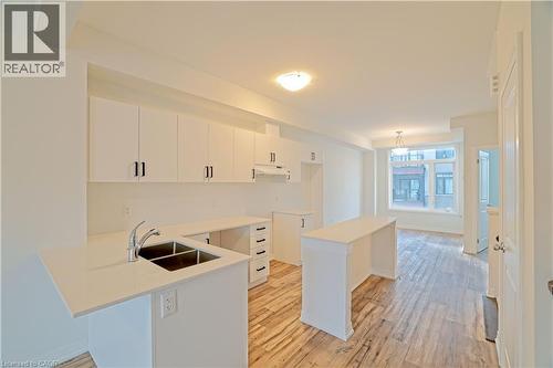 Kitchen with white cabinetry, light wood-style flooring, a breakfast bar, and a peninsula - 155 Equestrian Way Unit# 114, Cambridge, ON - Indoor Photo Showing Kitchen With Double Sink