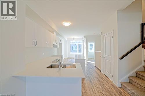 Kitchen with white cabinetry, light wood-type flooring, a peninsula, light stone countertops, and a breakfast bar - 155 Equestrian Way Unit# 114, Cambridge, ON - Indoor Photo Showing Kitchen With Double Sink