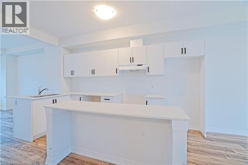 Kitchen featuring white cabinetry, light wood-style floors, a peninsula, and under cabinet range hood - 155 Equestrian Way Unit# 114, Cambridge, ON - Indoor Photo Showing Kitchen