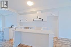 Kitchen featuring white cabinetry, light wood-style floors, a peninsula, and under cabinet range hood - 