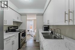Kitchen featuring stainless steel appliances, white cabinetry, light countertops, under cabinet range hood, and dark wood-type flooring - 