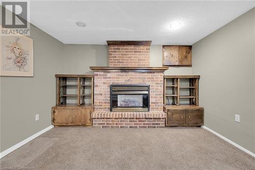Unfurnished living room with carpet flooring, a brick fireplace, baseboards, and a textured ceiling - 9 Gavin Drive, St. Catharines, ON - Indoor With Fireplace