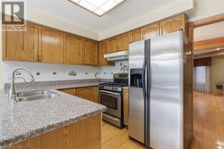 Kitchen with appliances with stainless steel finishes, light stone countertops, decorative backsplash, light wood finished floors, and brown cabinets - 