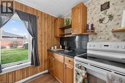 Kitchen with white electric range oven, dark countertops, open shelves, brown cabinets, and wood walls - 