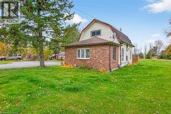 View of side of home with a gambrel roof, brick siding, a lawn, and roof with shingles - 
