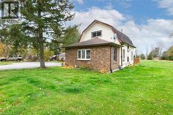 View of property exterior featuring a gambrel roof, brick siding, a yard, and roof with shingles - 