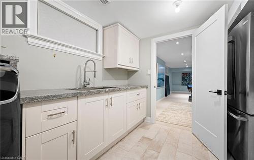Kitchen featuring freestanding refrigerator, light stone countertops, white cabinetry, and washer / dryer - 735 George Street, Burlington, ON - Indoor Photo Showing Kitchen