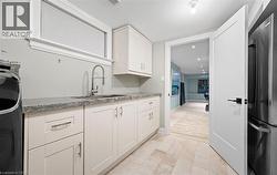 Kitchen featuring freestanding refrigerator, light stone countertops, white cabinetry, and washer / dryer - 
