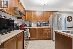 Kitchen featuring stainless steel appliances, brown cabinetry, under cabinet range hood, light countertops, and light tile patterned floors - 