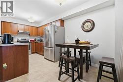 Kitchen featuring appliances with stainless steel finishes, brown cabinetry, light countertops, light tile patterned floors, and under cabinet range hood - 