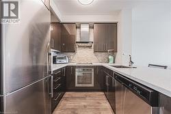 Kitchen featuring light wood-style flooring, a toaster, a sink, appliances with stainless steel finishes, and wall chimney range hood - 
