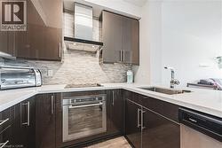 Kitchen featuring a sink, stainless steel appliances, dark brown cabinetry, wall chimney range hood, and tasteful backsplash - 