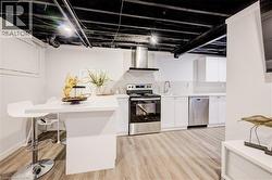 Kitchen with stainless steel appliances, wall chimney exhaust hood, light wood-style flooring, and white cabinets - 