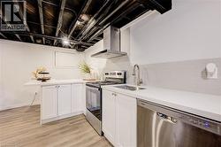 Kitchen with appliances with stainless steel finishes, white cabinetry, wall chimney range hood, light wood-type flooring, and decorative backsplash - 