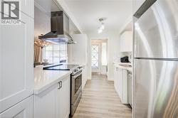 Kitchen with appliances with stainless steel finishes, white cabinetry, ventilation hood, hanging light fixtures, and light wood-style floors - 
