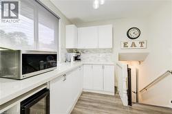 Kitchen with stainless steel microwave, white cabinetry, light wood-type flooring, backsplash, and light stone counters - 