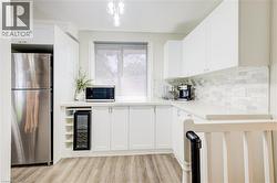 Kitchen featuring freestanding refrigerator, white cabinetry, light wood-style floors, beverage cooler, and tasteful backsplash - 