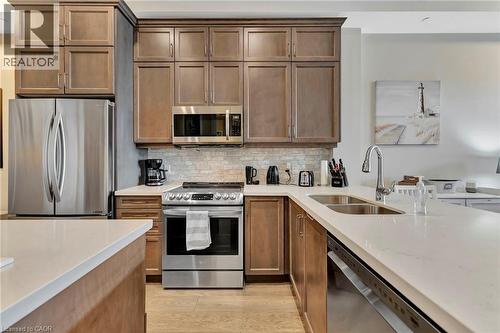 Kitchen with stainless steel appliances, light stone counters, decorative backsplash, and light wood-type flooring - 85B Morrell Street Unit# 117, Brantford, ON - Indoor Photo Showing Kitchen With Double Sink