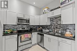 Kitchen featuring backsplash, a sink, white cabinetry, stainless steel appliances, and dark countertops - 