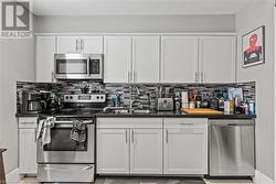 Kitchen with backsplash, a sink, white cabinetry, stainless steel appliances, and dark countertops - 