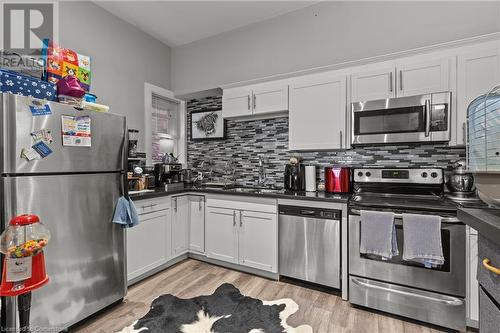 Kitchen with stainless steel appliances, backsplash, a sink, dark countertops, and light wood finished floors - 181 West Avenue N, Hamilton, ON - Indoor Photo Showing Kitchen With Upgraded Kitchen