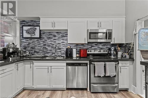 Kitchen with white cabinets, dark countertops, appliances with stainless steel finishes, a sink, and light wood-type flooring - 181 West Avenue N, Hamilton, ON - Indoor Photo Showing Kitchen With Double Sink With Upgraded Kitchen