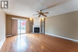Unfurnished living room with a large fireplace, a textured ceiling, light wood-type flooring, and ceiling fan - 
