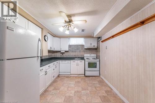 Kitchen with white appliances, dark countertops, white cabinets, backsplash, and a textured ceiling - 162 Solomon Crescent, Hamilton, ON - Indoor Photo Showing Kitchen