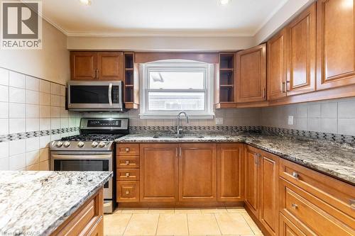 Kitchen with brown cabinets, stainless steel appliances, dark stone counters, open shelves, and crown molding - 162 Solomon Crescent, Hamilton, ON - Indoor Photo Showing Kitchen