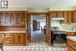 Kitchen featuring brown cabinetry, stainless steel range with electric cooktop, french doors, light countertops, and under cabinet range hood - 