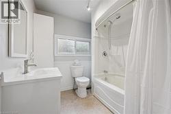 Full bathroom featuring shower / bath combo with shower curtain, vanity, wainscoting, and light tile patterned flooring - 