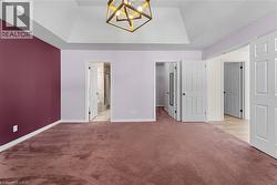 Unfurnished bedroom featuring a raised ceiling, a chandelier, a walk in closet, carpet, and ensuite bath - 