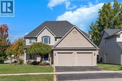 Traditional home featuring a front yard, roof with shingles, driveway, brick siding, and an attached garage - 