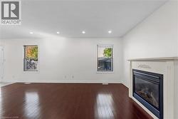 Unfurnished living room featuring plenty of natural light, dark wood-style flooring, a glass covered fireplace, and recessed lighting - 