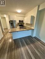 Kitchen with white cabinetry, stainless steel appliances, a textured ceiling, dark wood finished floors, and dark stone countertops - 