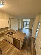 Kitchen featuring a Island, stainless steel dishwasher, dark wood finished floors, light stone counters, and a textured ceiling - 
