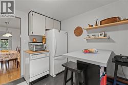 Kitchen featuring white appliances, open shelves, a kitchen bar, white cabinetry, and light countertops - 