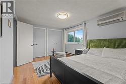 Bedroom with a textured ceiling, light wood-style flooring, an AC wall unit, a closet, and a baseboard radiator - 